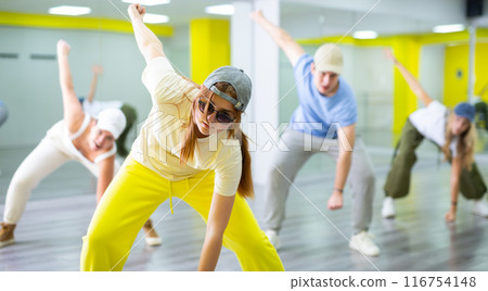 Excited positive teenage dancers having fun and learning modern dance during class in modern hall 116754148