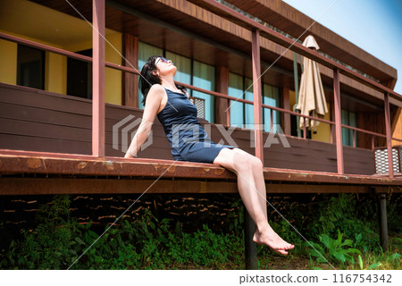 50 years old russian woman in short dress and sunglasses sitting on a balcony and enjoying on the summer day  116754342
