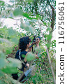 a male photographer in the wild with his camera with leaves foreground 116756061