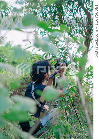 a male photographer in the wild with his camera with leaves foreground a male photographer in the wild with his camera with leaves foreground 116756061