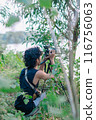 a male photographer in the wild with his camera with leaves foreground 116756063