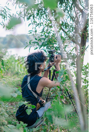 a male photographer in the wild with his camera with leaves foreground a male photographer in the wild with his camera with leaves foreground 116756063