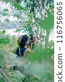 a male photographer in the wild with his camera with leaves foreground 116756065