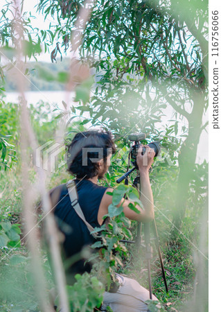 a male photographer in the wild with his camera with leaves foreground a male photographer in the wild with his camera with leaves foreground 116756066