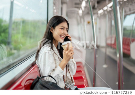 A beautiful, happy young Asian female passenger is talking on the phone while sitting in a sky train 116757289