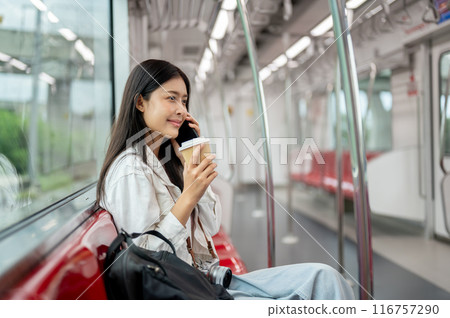 A beautiful Asian female is sipping coffee and talking on the phone while commuting on a sky train. A beautiful Asian female is sipping coffee and talking on the phone while commuting on a sky train. 116757290
