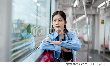 A positive, thoughtful Asian female is gazing at the view outside while commuting by sky train. A positive, thoughtful Asian female is gazing at the view outside while commuting by sky train. 116757315