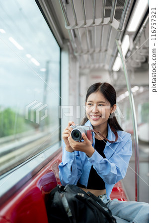A happy Asian female traveller is enjoying taking pictures with her camera on a sky train. 116757321