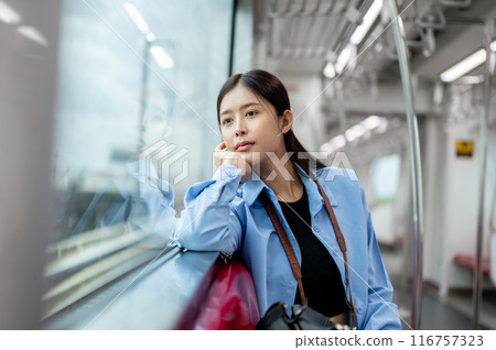 A positive, thoughtful Asian female is gazing at the view outside while commuting by sky train. A positive, thoughtful Asian female is gazing at the view outside while commuting by sky train. 116757323