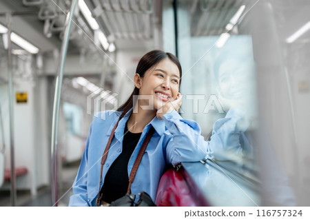 A happy, smiling Asian female is gazing at the view outside while commuting by sky train. 116757324