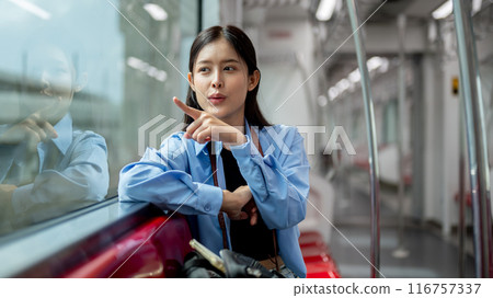 A cheerful Asian woman is enjoying the view outside while sitting on a seat in a sky train. A cheerful Asian woman is enjoying the view outside while sitting on a seat in a sky train. 116757337