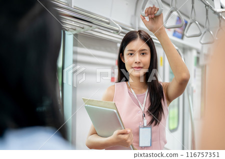 A charming Asian female office employee is holding a handrail while commuting by sky train to work. 116757351
