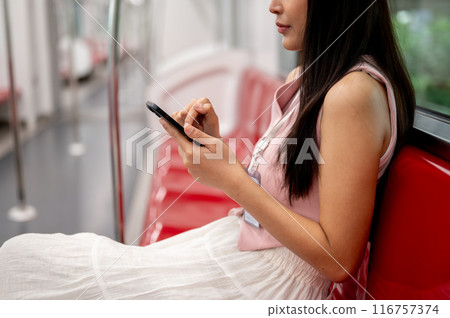 Thoughtful Asian female sitting at a seat, reading messages on her phone while taking the sky train. Thoughtful Asian female sitting at a seat, reading messages on her phone while taking the sky train. 116757374