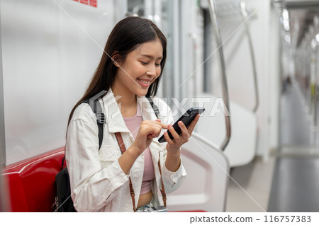 A happy Asian female tourist is chatting on the phone while sitting on a sky train or underground. A happy Asian female tourist is chatting on the phone while sitting on a sky train or underground. 116757383