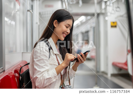 A happy Asian female tourist is chatting on the phone while sitting on a sky train or underground. A happy Asian female tourist is chatting on the phone while sitting on a sky train or underground. 116757384