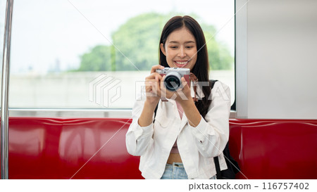 An Asian female tourist is taking pictures with her camera while commuting in a city on a sky train. An Asian female tourist is taking pictures with her camera while commuting in a city on a sky train. 116757402