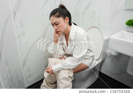 stress woman have problems while sitting on a toilet bowl in bathroom 116758388