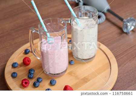 Milkshake in glass with tube on wooden stand. Raspberries and blueberries. Healthy food and nutrition.  116758661