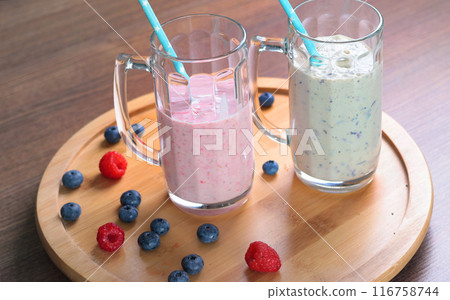 Milkshake in glass with tube on wooden stand. Raspberries and blueberries. Healthy food and nutrition.  116758744