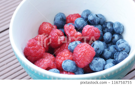 Fresh berries in ceramic bowl. Blueberries and raspberries. Healthy Lifestyle. Nature and harvest in summer.  116758755