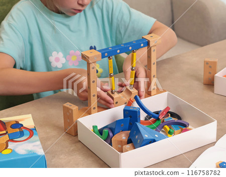 Girl assembles swing from magnetic wooden construction set. Toys and activiti children. Developmental activities at home. Girl assembles swing from magnetic wooden construction set. Toys and activiti children. Developmental activities at home. 116758782