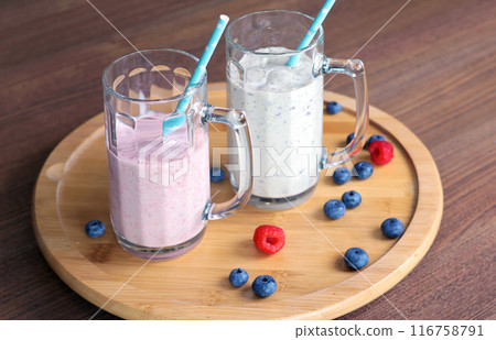 Milkshake in glass with tube on wooden stand. Raspberries and blueberries. Healthy food and nutrition.  116758791