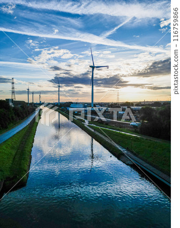 Wind turbines are installed along a canal, creating reflections under a scenic sunset sky 116759866