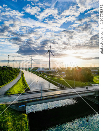 Wind turbines demonstrate clean energy tech, providing a picturesque view at sunset near a canal Wind turbines demonstrate clean energy tech, providing a picturesque view at sunset near a canal 116759871