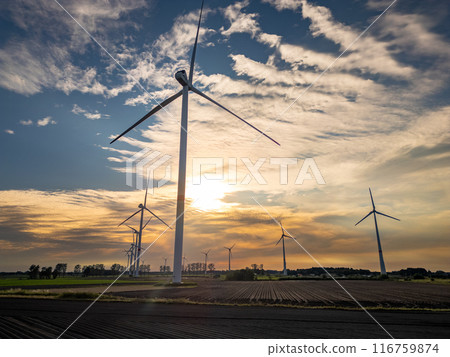 In an open field, wind turbines generate clean energy against a sunset backdrop In an open field, wind turbines generate clean energy against a sunset backdrop 116759874