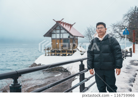man tourist sightseeing Kansa Shrine and Lake Tazawa in winter. Traveler travel in Semboku city, Akita Prefecture, Japan. Landmark for tourist attraction in Tohoku region. Japan travel and vacation. 116759966