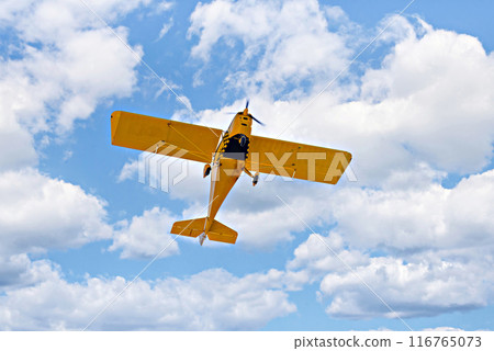 Yellow single-engine ultralight airplane flying in the blue sky with white clouds Yellow single-engine ultralight airplane flying in the blue sky with white clouds 116765073