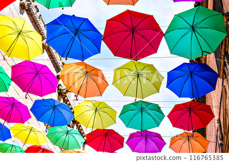 Background of many hanging colorful umbrellas decorating the street of a town Background of many hanging colorful umbrellas decorating the street of a town 116765385