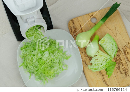 Cabbage and onion in a vegetable cutter on kitchen table. Chopped cabbage is falling from grinder into a bowl. Homemade healthy food. Health line. 116766114