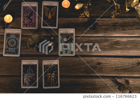 Tarot cards including The Fool and The Lovers alongside crystals and candles on a textured wooden table. 116766623