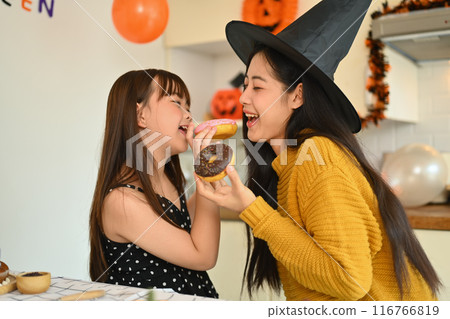 Cute little girl and mother eating sweet donut in kitchen. Halloween celebration concept 116766819