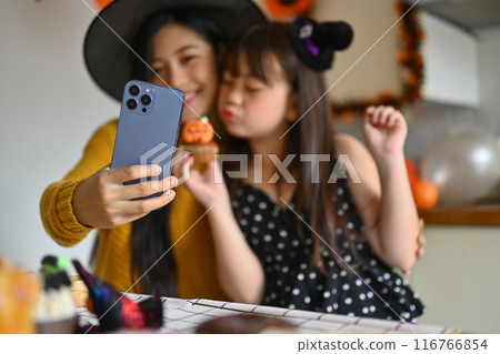 Happy mother and her little daughter taking a selfie on smart phone in Halloween decorated kitchen 116766854