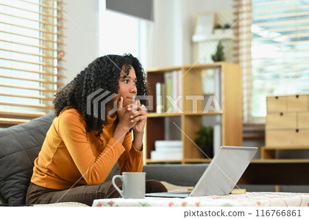 Thoughtful African American woman sitting on couch and looking away, dreaming or thinking of something Thoughtful African American woman sitting on couch and looking away, dreaming or thinking of something 116766861