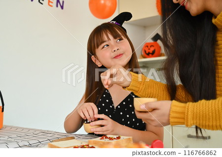 Mother and daughter decorating Halloween cupcakes in the decorated kitchen 116766862