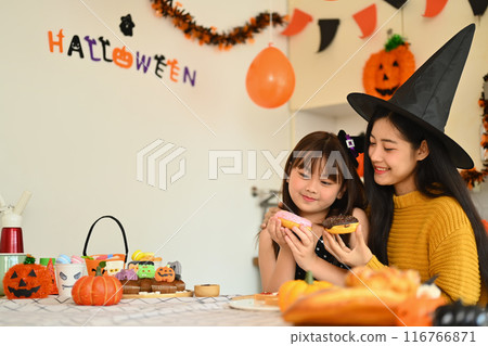 Cute little girl and mother eating sweet donut in kitchen. Halloween celebration concept 116766871