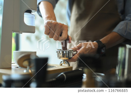 Hand of barista using a tamper to press ground coffee, making an espresso in coffee shop 116766885