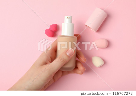 Bottle with foundation in female hand and cosmetic sponges on pink background, top view Bottle with foundation in female hand and cosmetic sponges on pink background, top view 116767272