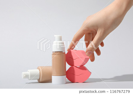 Bottles with foundation, female hand and cosmetic sponges on white background 116767279