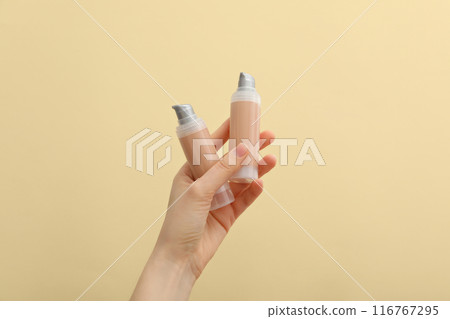 Bottles with foundation in female hands on beige background Bottles with foundation in female hands on beige background 116767295