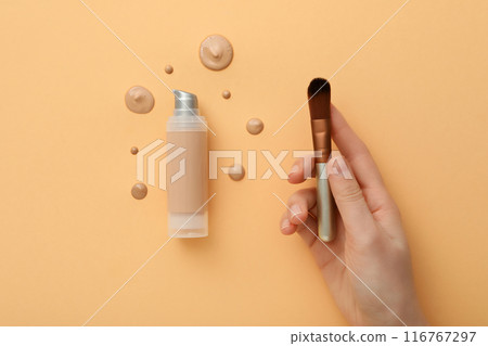 Cosmetic brush in female hand, bottle and drops of foundation on beige background, top view Cosmetic brush in female hand, bottle and drops of foundation on beige background, top view 116767297