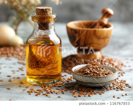 Glass bottle flaxseed oil, placed beside small bowl of flax seeds on light colored surface 116767853