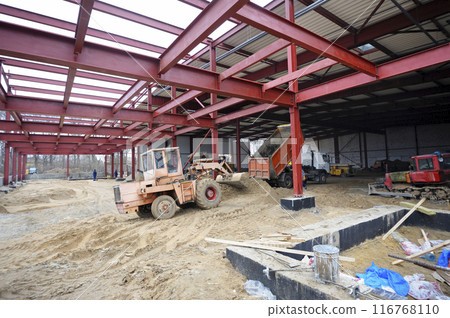 Construction of the hangar. Backhoe working, truck uloading sand Construction of the hangar. Backhoe working, truck uloading sand 116768110