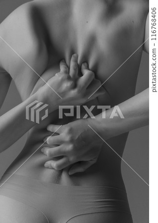 Monochrome photo of woman's back showcasing her hands tightly gripping skin of body part. Texture of skin and muscle definition. Monochrome photo of woman's back showcasing her hands tightly gripping skin of body part. Texture of skin and muscle definition. 116768406