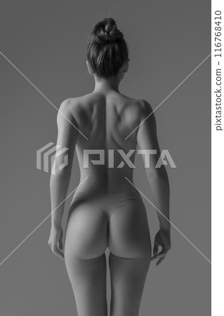 Rear view photo of young fit woman posing naked demonstrate her posture and healthy back. Black and white filter. 116768410