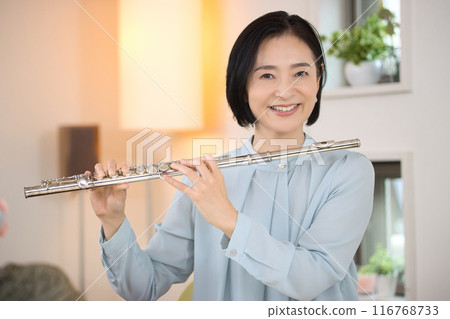 Middle-aged woman playing the flute in the living room 116768733