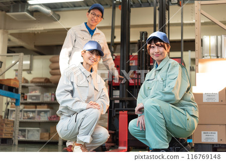 Three workers in work clothes, men and women, gather in front of a forklift 116769148